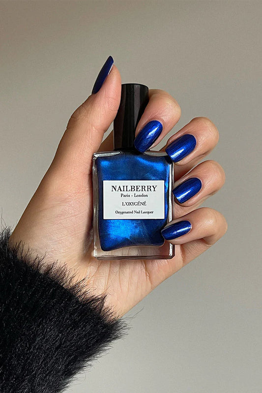 Hand with light skin tone holding Nailberry Blue Moon – soft, vegan pastel blue polish for elegant, fresh nail looks