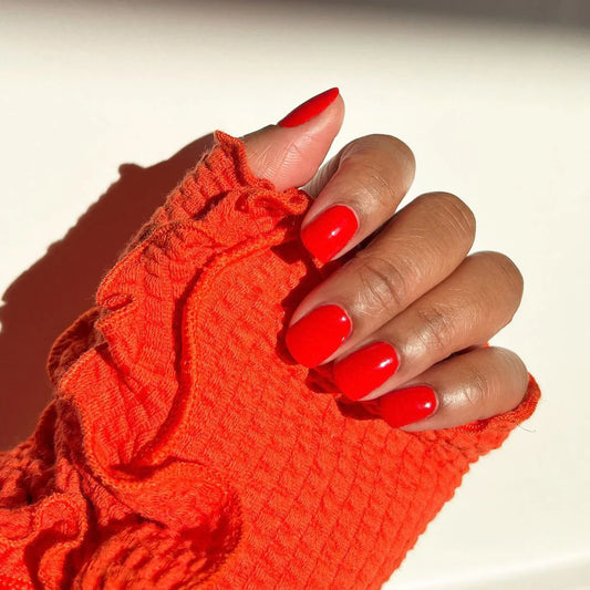 Hand with light skin tone wearing Bio Sculpture Blazing Lacquer – vegan, bright orange-red polish for a vibrant, energetic nail look