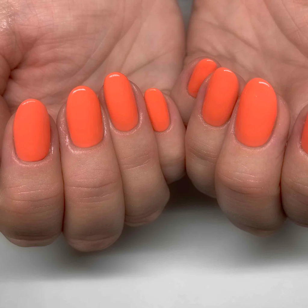 Hand wearing Bio Sculpture Gemini Nail Polish No. 2002 Coral – vegan, bright orange coral polish for a vibrant, cheerful nail look
