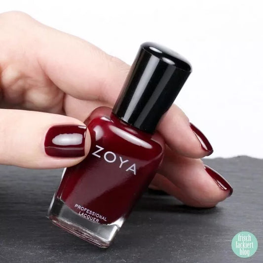 Hand holding Zoya Dakota nail polish – vegan, deep red polish bottle for stylish, modern manicures
