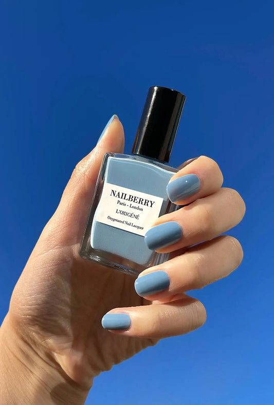Hand with light skin tone holding Nailberry Mistral Breeze – gentle, vegan pastel blue polish for elegant, natural-looking manicures