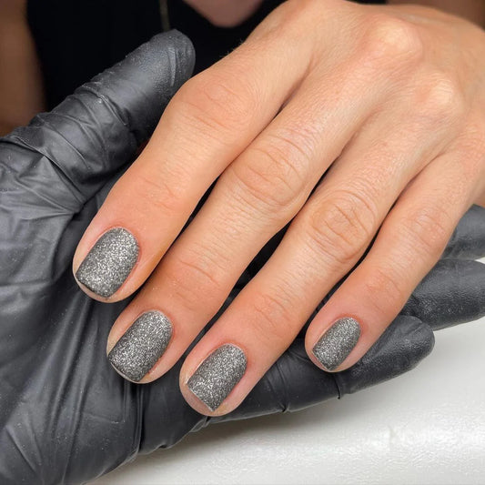 Hand with light skin tone wearing Bio Sculpture Gemini Nail Polish No. 252 Starlit Cobblestone – vegan, solid glittery black polish for a chic, statement nail look