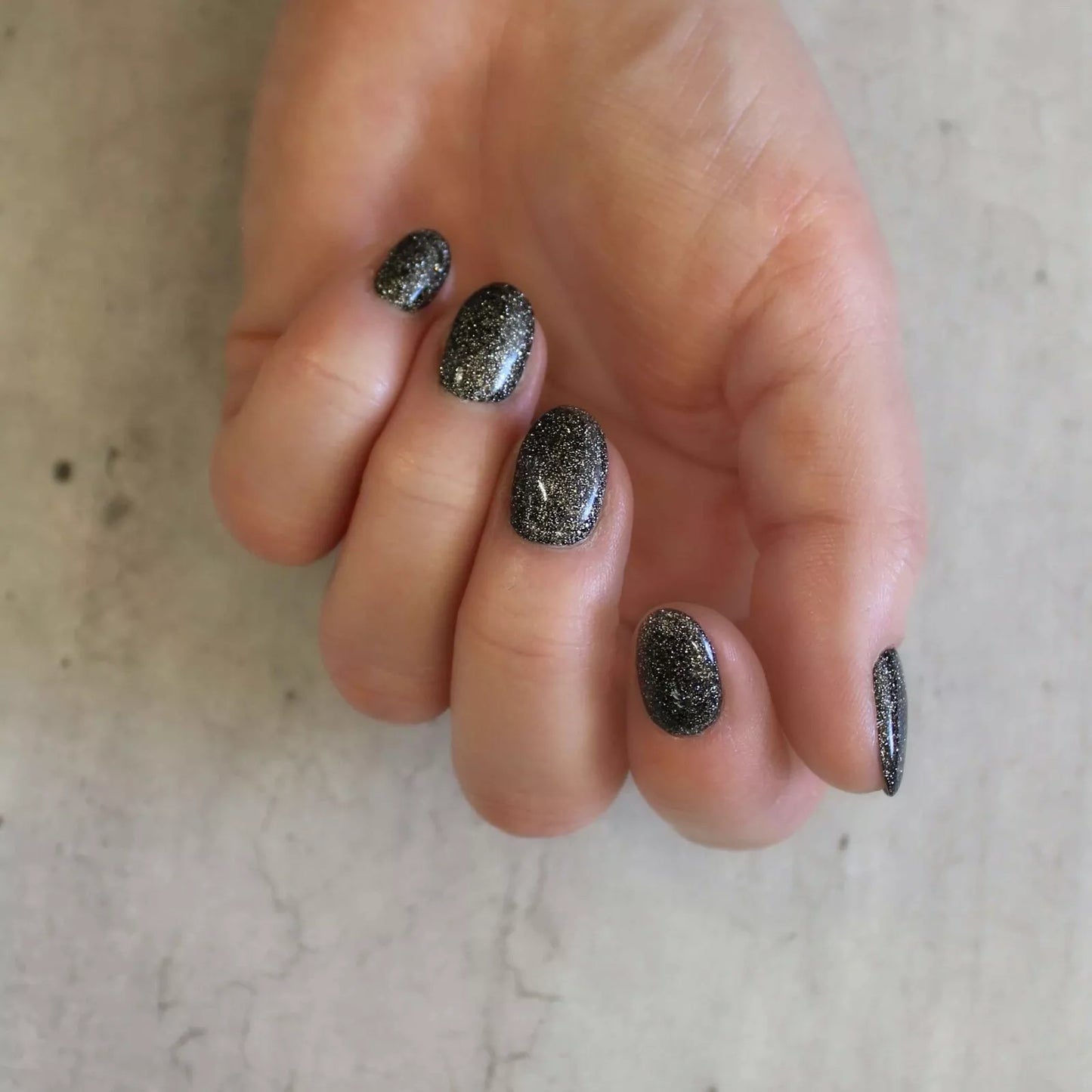Hand wearing Bio Sculpture Gemini Nail Polish No. 252 Starlit Cobblestone – bold, vegan solid glittery black polish for inclusive, dazzling manicures