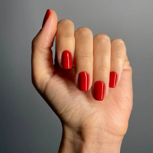 Fingers painted with Gemini Sunset Red on light skin – breathable, vibrant red polish for everyday elegance