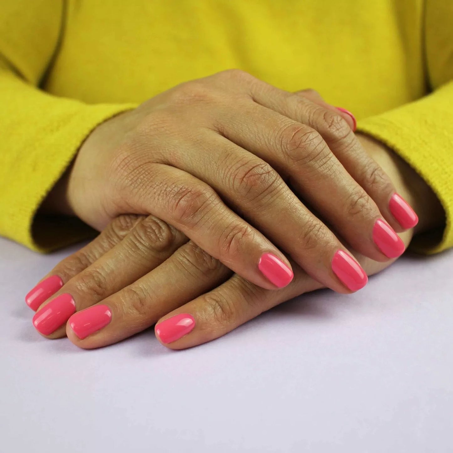 Hand wearing Bio Sculpture Gemini Nail Polish No. 75 Fruity Tooty – bold, vegan bright coral pink polish for inclusive, striking manicures