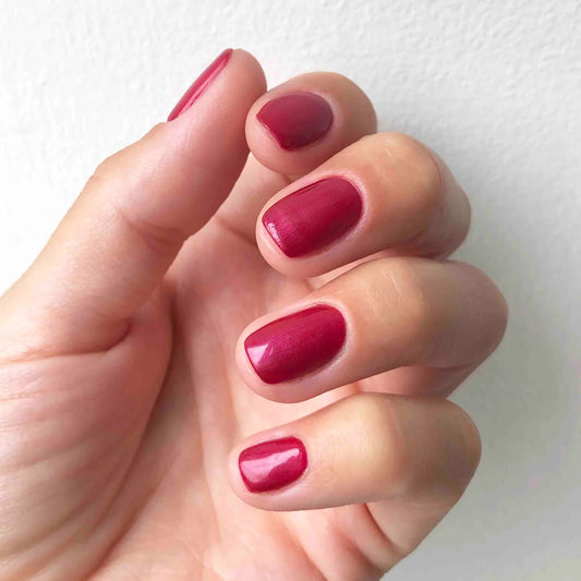 Hand wearing Bio Sculpture Gemini Nail Polish No. 22 Ravishing Red – vegan, pearlescent cherry red polish for a chic, radiant nail look
