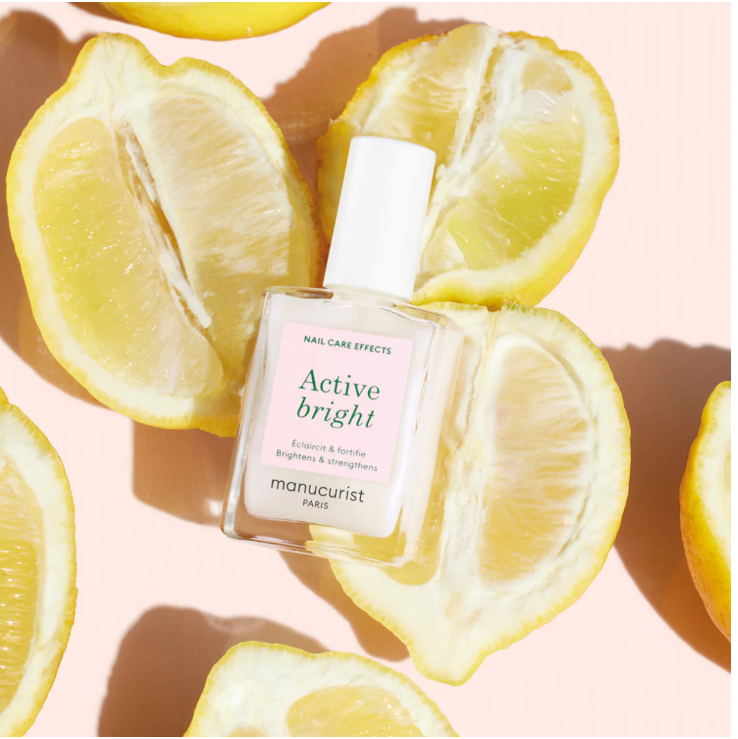 Manucurist Base Coat Active Bright bottle displayed on fresh lemons – vegan, citrus-infused brightening base coat for radiant nails
