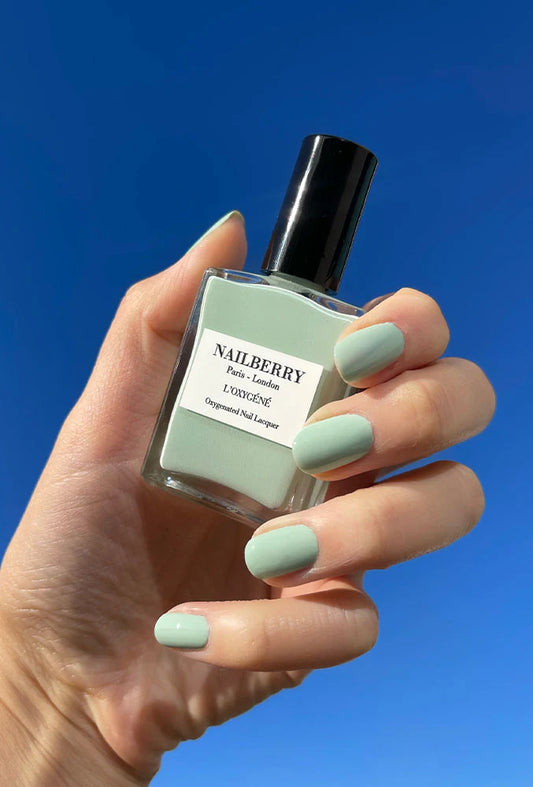 Hand holding the polish bottle with light skin tone wearing Nailberry Wild Sage – gentle, vegan sage green polish for elegant, natural-looking manicures