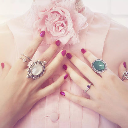 Elegant hands adorned with rings, showcasing vibrant pink manicure against a soft pink blouse.
