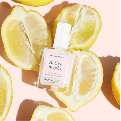 Manucurist Base Coat Active Bright bottle displayed on fresh lemons – vegan, citrus-infused brightening base coat for radiant nails